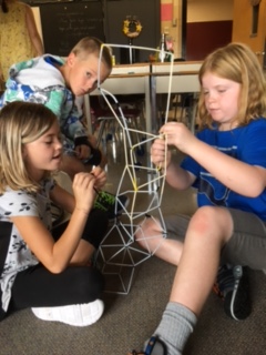 Two female students work with pipe cleaners to build a tower