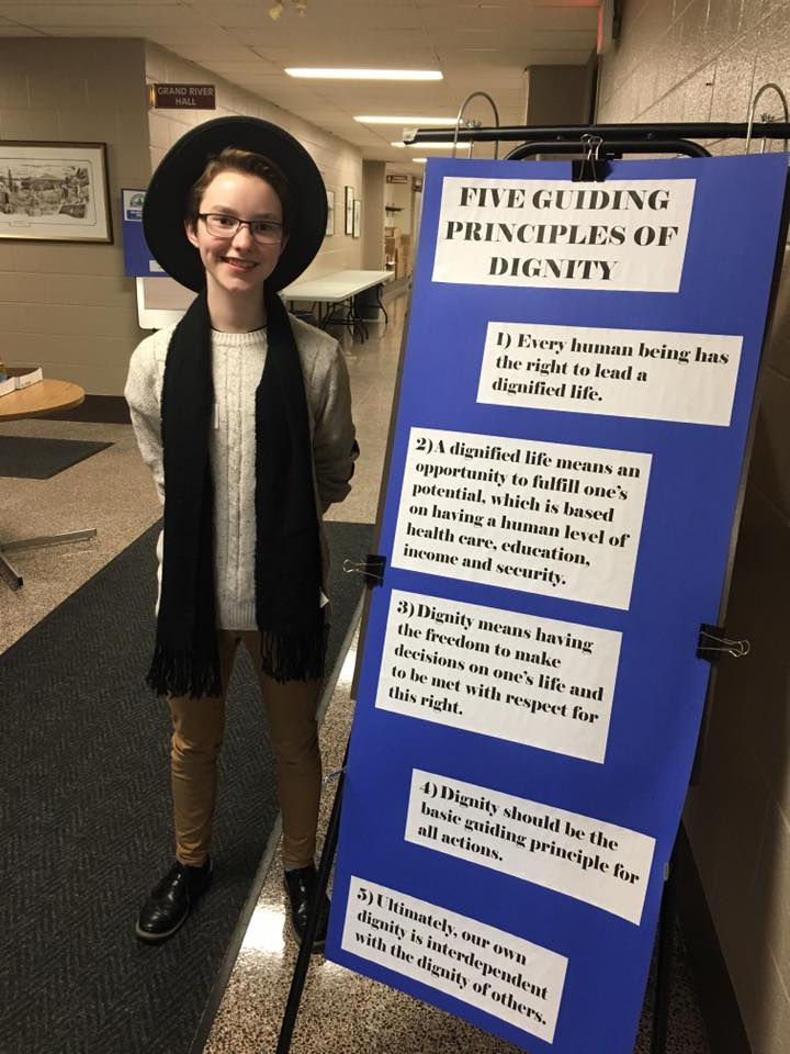 A student poses with a poster indicating the principles of dignity
