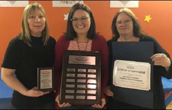 Teachers smile while holding a plaque