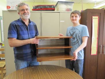 A student and teacher hold up a completed woodworking project