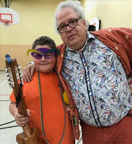 A sharply dressed musician poses with a young student wearing Mardi Gras beads