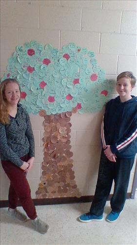 Two students stand on either side of a paper tree display with messages written on the leaves