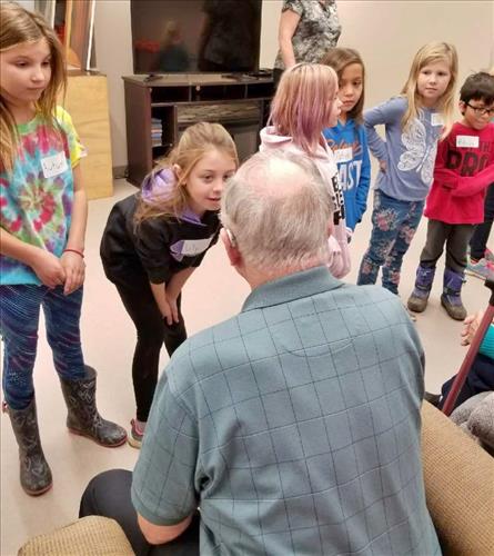 A group of elementary students converses with older adults at a retirement home