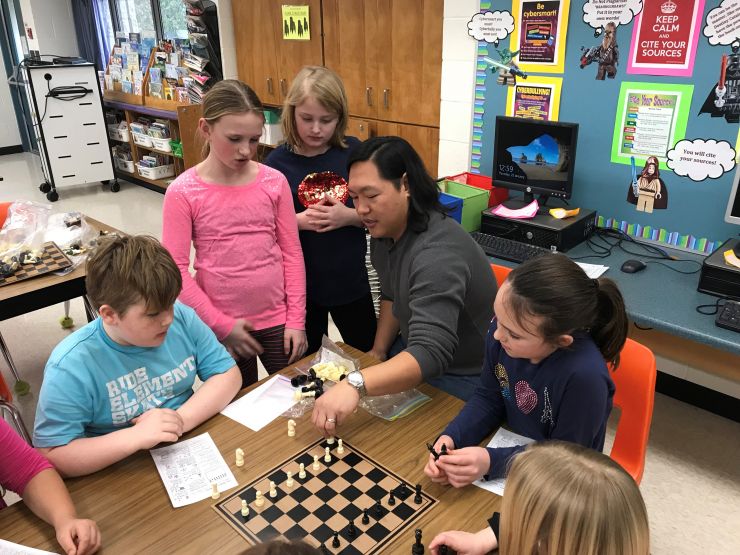 Students watch and listen as community volunteer leads chess lesson