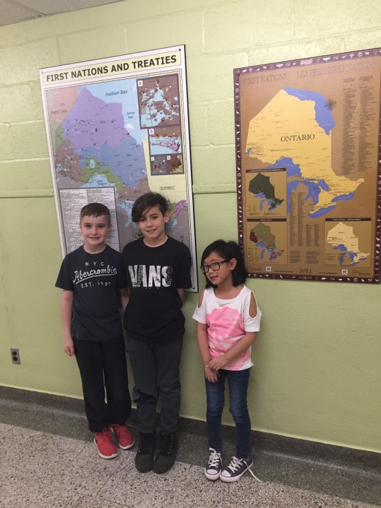 Three students stand under a poster of a map depicting First Nations treaties