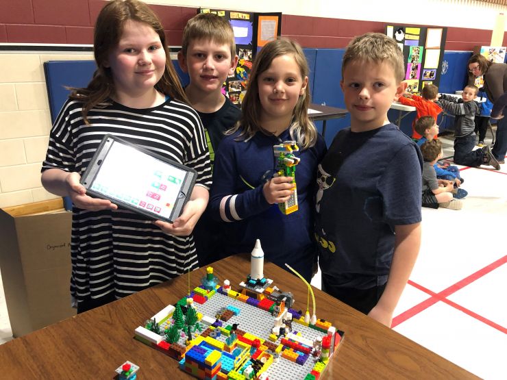 Four students proudly display a completed Lego model