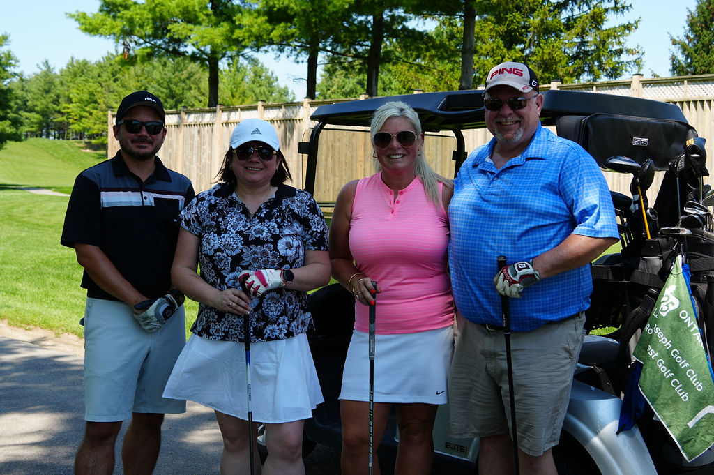 People smiling with golf clubs in front of golf cart
