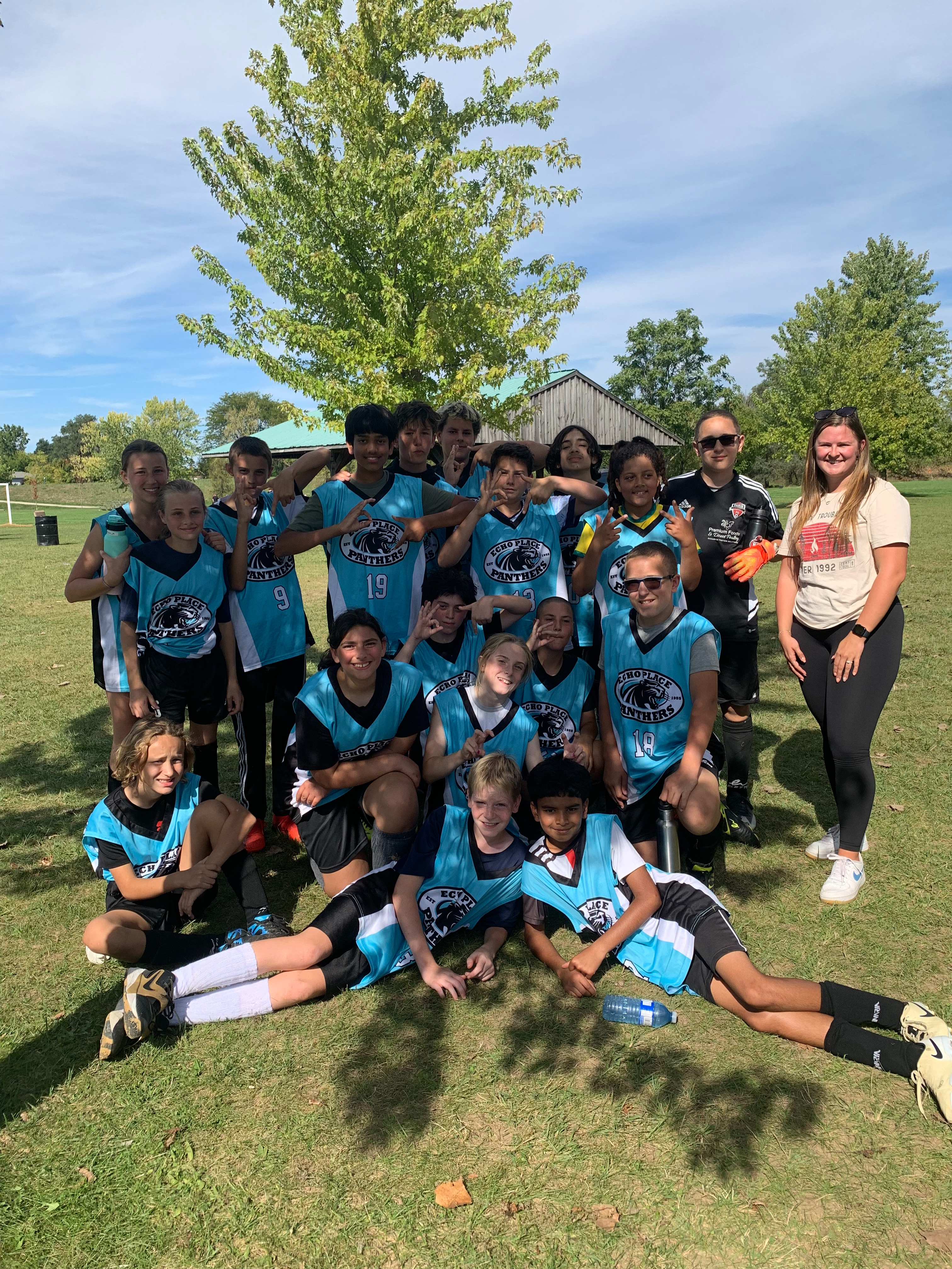 The intermediate soccer team is posing under a tree together with their school jersey's on.